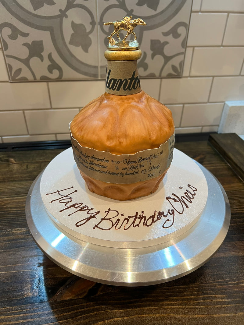 Birthday cake designed to look like a bottle of Blanton's bottle on a wooden table.