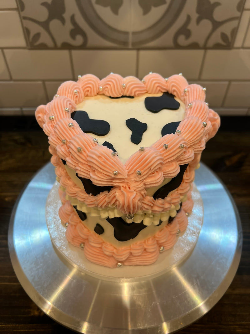 Two-tiered cake with pink and black cow print design on a metal cake stand.