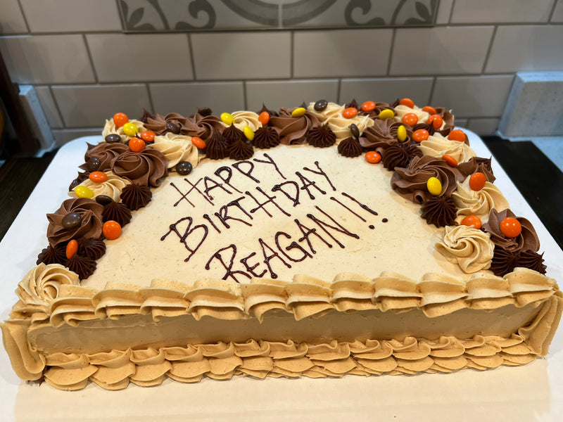 Birthday cake with 'Happy Birthday Reagan!' written on it, placed on a white surface.