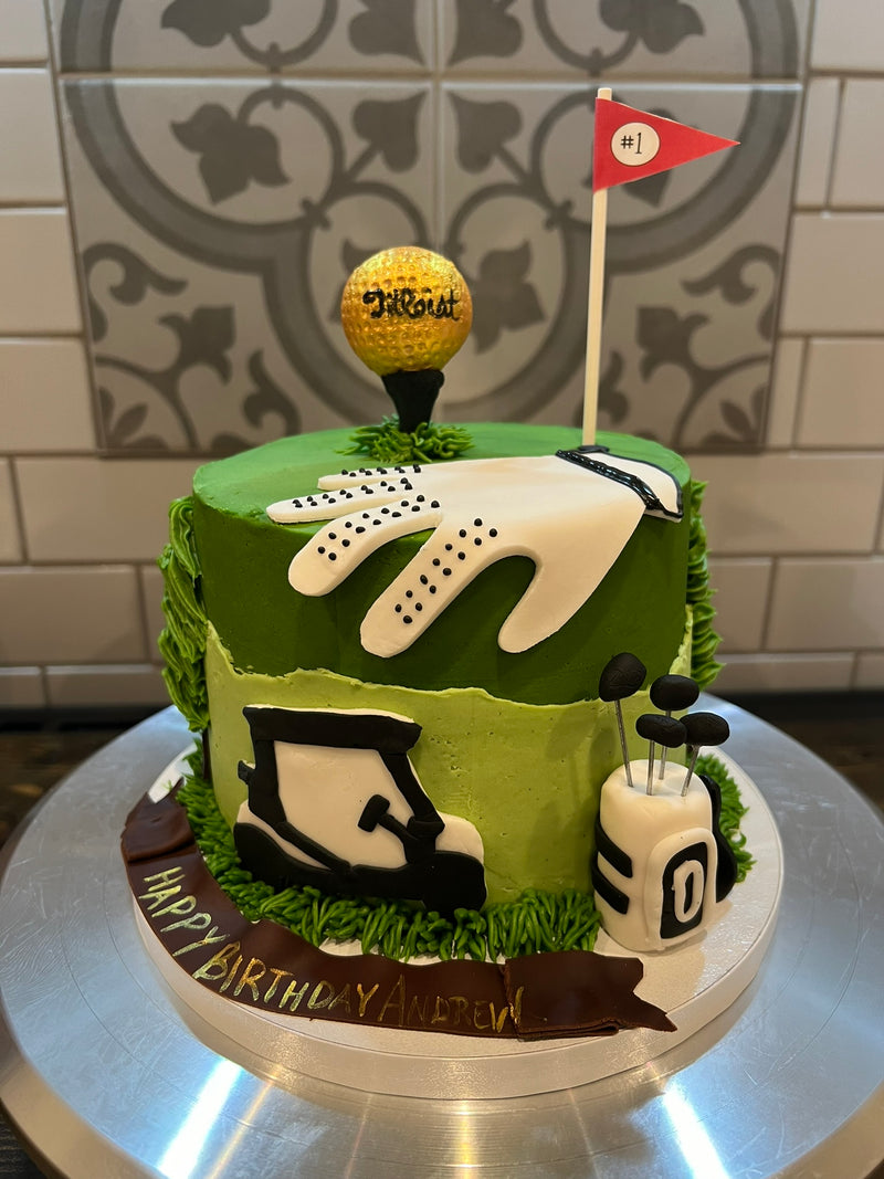 Golf-themed birthday cake with green icing, golf glove, ball, and flag on a silver cake stand.