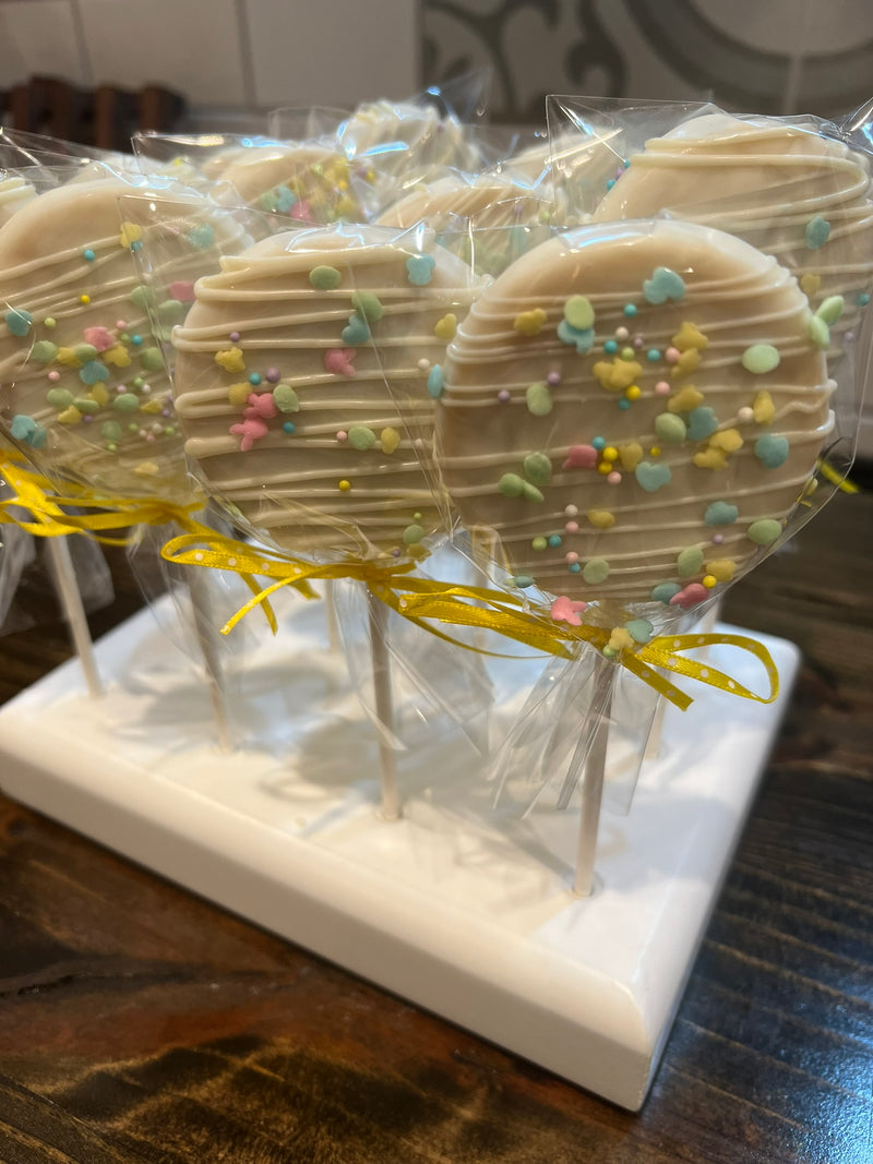 White chocolate-covered lollipops with colorful sprinkles on a white stand.