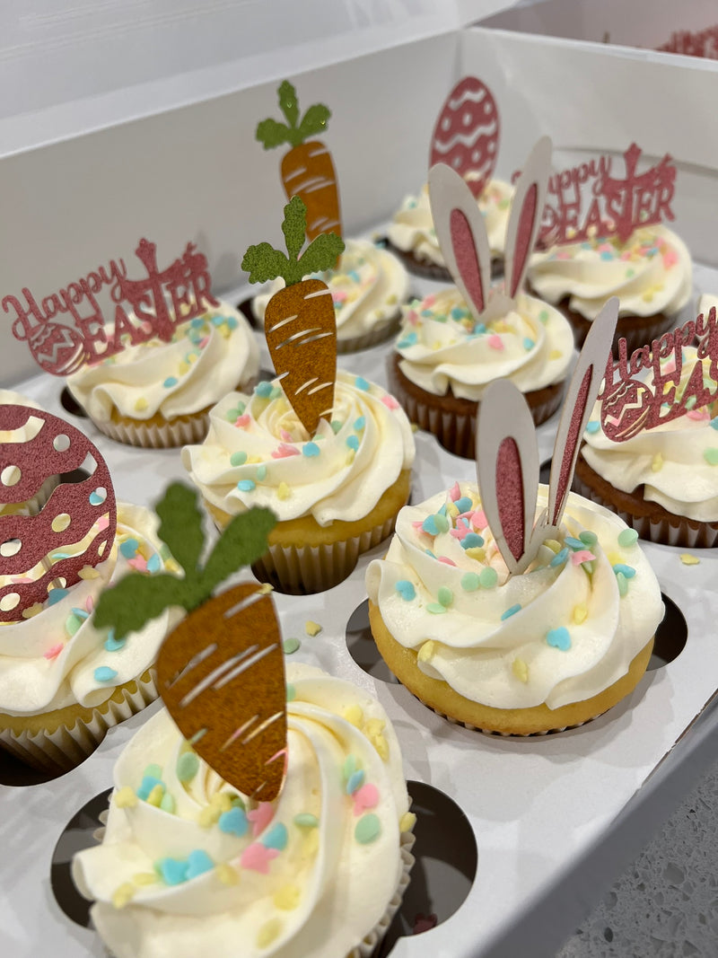 Cupcakes decorated with Easter-themed toppers including carrots and bunny ears on a white tray.