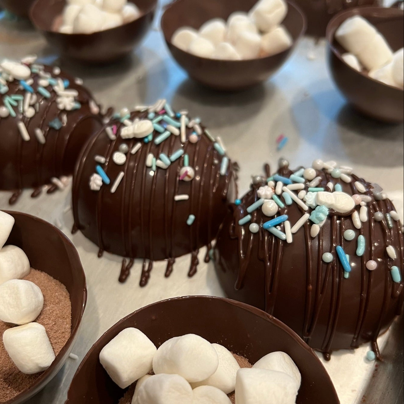 Chocolate bowls filled with marshmallows and sprinkles on a metal surface