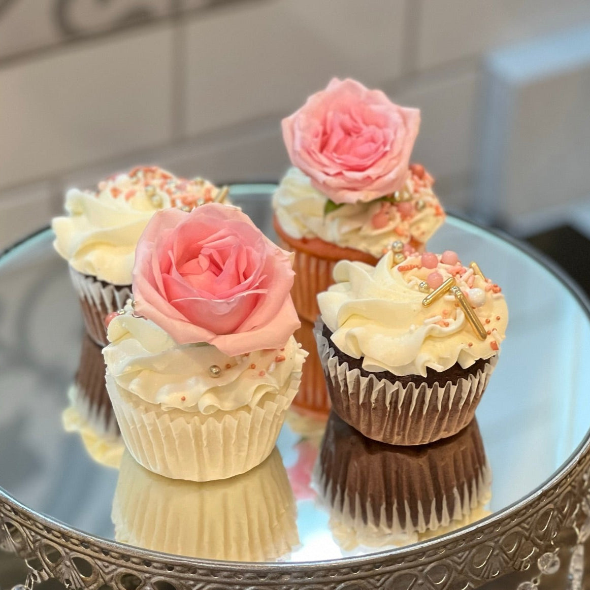Decorative cupcakes with pink roses on a silver cake stand.