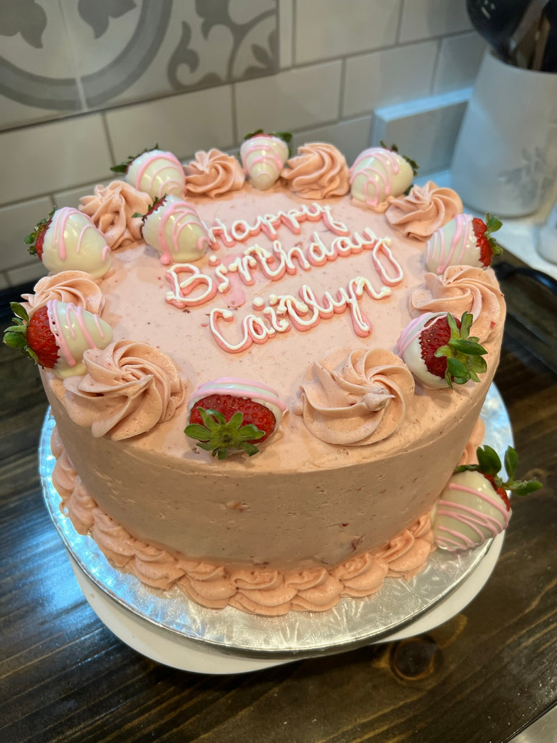 Birthday cake with pink frosting, strawberries, and 'Happy Birthday Caitlyn' text on a kitchen counter.